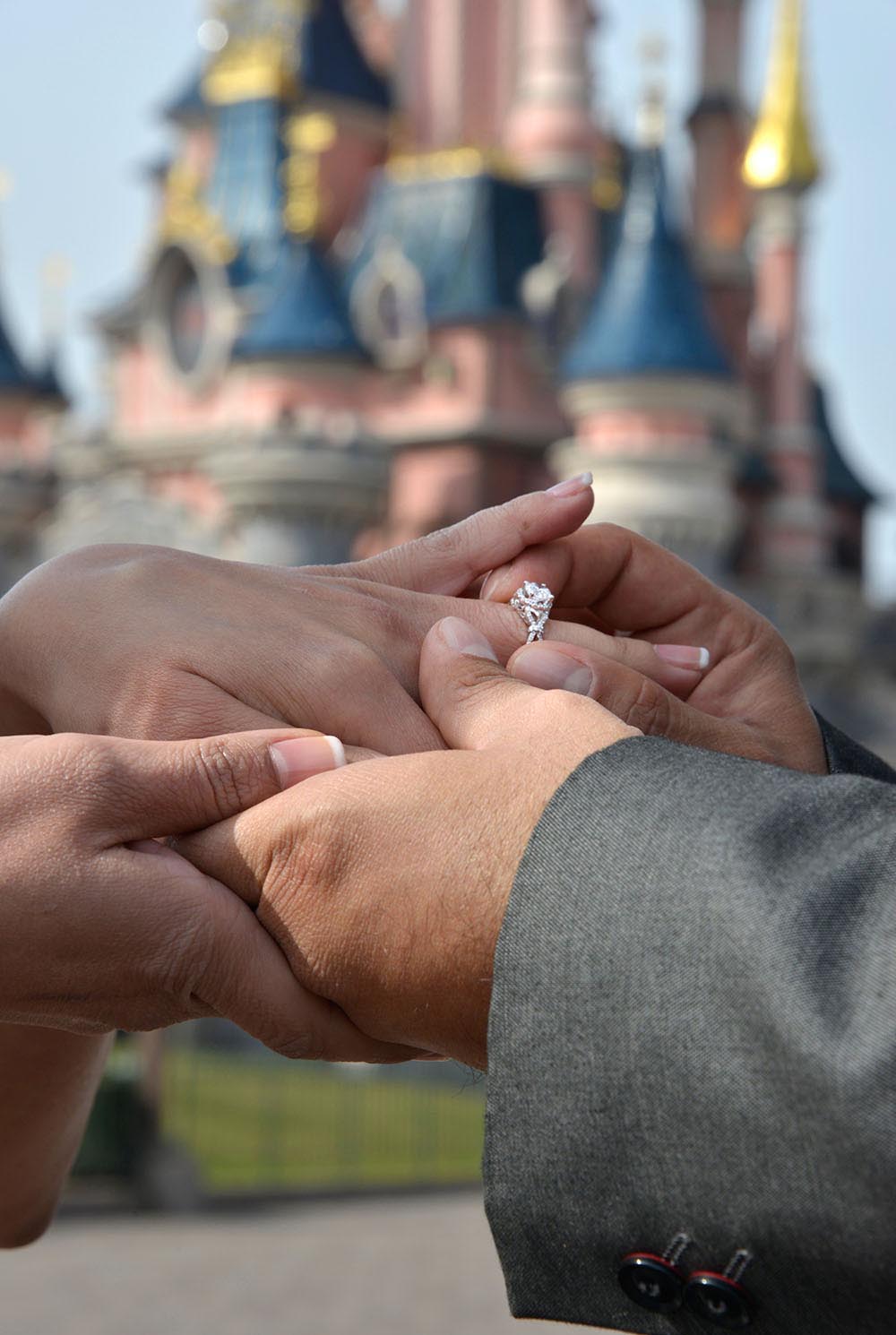 Groom putting engagement ring on bride fingers with EuroDisney backdrop